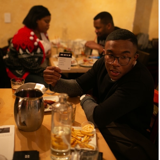 Friends at a restaurant reading a One Gotta Go card out loud